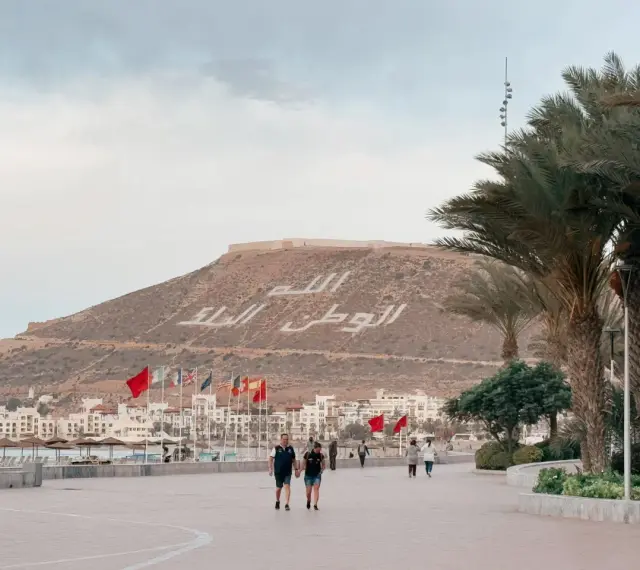 Spacerem po promenadzie w Agadirze, z widokiem na miasto i napisem na wzgórzu. Czy Agadir jest bezpieczny? Tak, wygląda na spokojne miejsce.