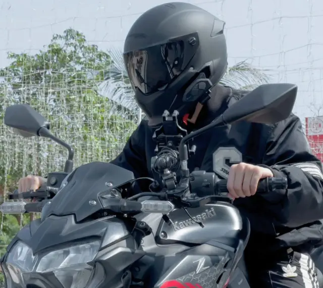 Motocyklista w kasku siedzi na motocyklu Kawasaki, z zamontowanym interkomem na kasku.