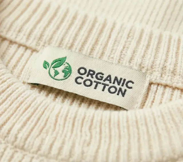 Metka z napisem "ORGANIC COTTON" na kremowym swetrze z prążkowanej dzianiny. To świadczy o tym, że cotton to materiał ekologiczny.
