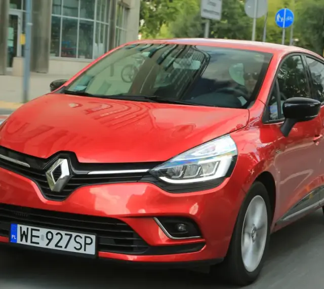 Czerwony Renault Clio 3 1.2 benzyna w ruchu miejskim. Kierowca w okularach przeciwsłonecznych.
