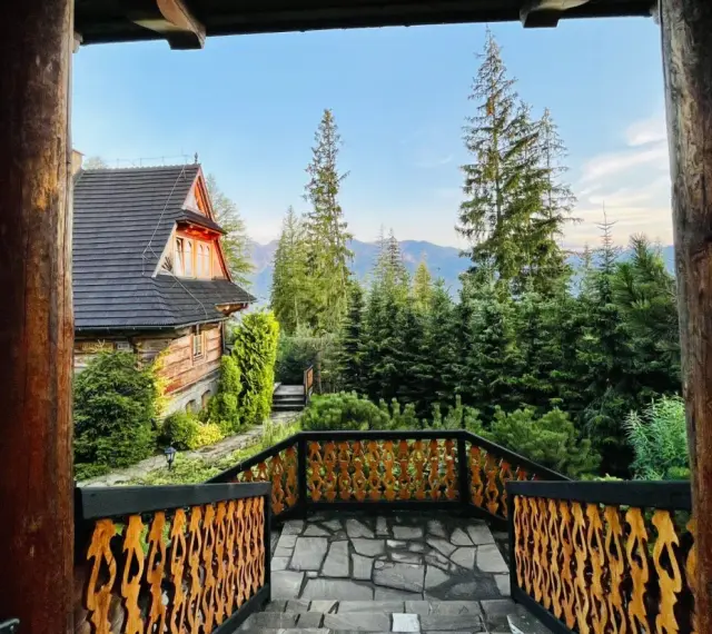 Drewniany dom z widokiem na góry, otoczony lasem. Widok z tarasu z rzeźbioną balustradą, idealne miejsce na relaks w stylu Gubałówka Zakopane.