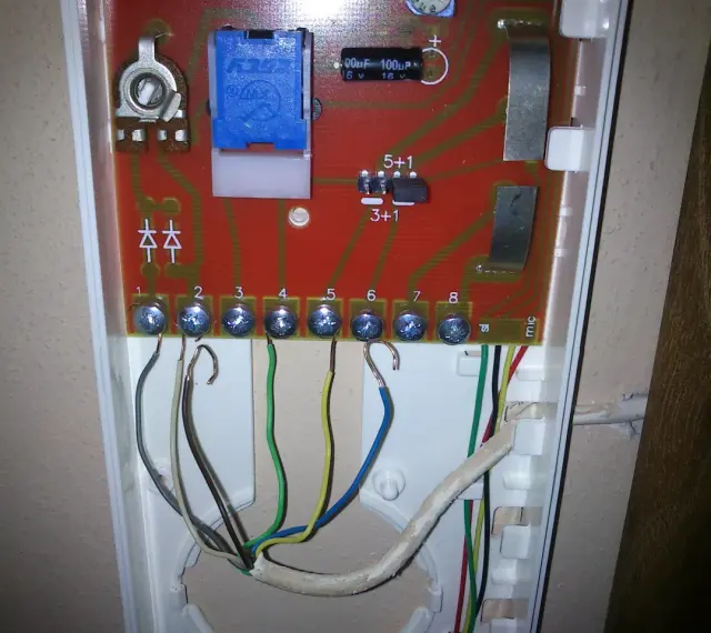 Schemat podłączenia domofonu w bloku 2 przewodowego. Widoczne zaciski śrubowe z podłączonymi przewodami, płytka drukowana z elementami elektronicznymi.