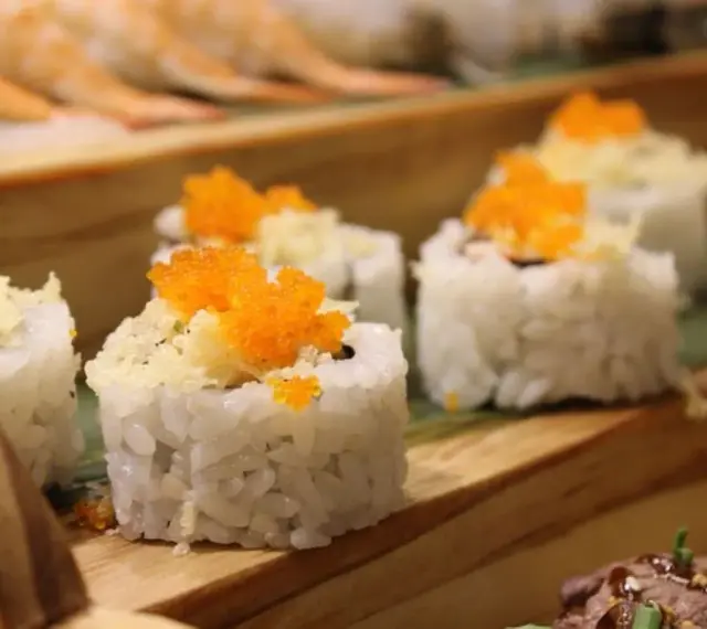 Roladki sushi z pomarańczową ikrą i chrupiącą posypką, idealne do słodkiego sosu do sushi.