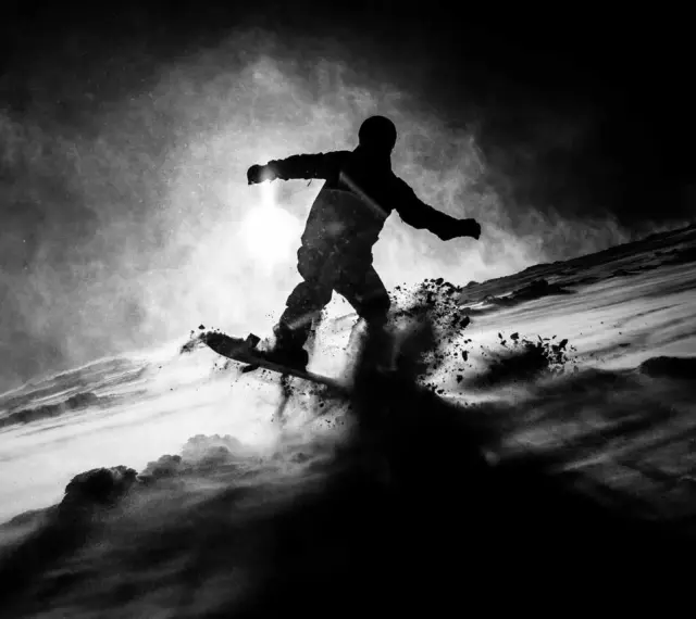 Une silhouette de snowboarder en plein saut, projetant de la neige. L'image, une peinture sur toile noire, capture l'énergie du mouvement dans un style dramatique.