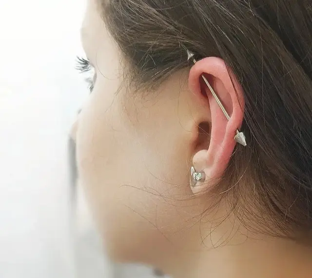 Industrialny piercing ucha z długą sztangą i dwoma stożkami. To przykład, co to jest piercing, który ozdabia ciało.