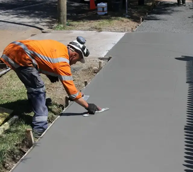 Robotnik w pomarańczowej kamizelce wygładza świeży beton. Zastanawiasz się, ile kosztuje kubik betonu na taki podjazd?
