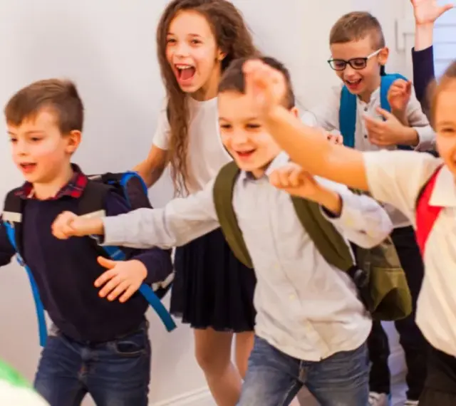 Fröhliche Schulkinder mit Rucksäcken rennen los.
