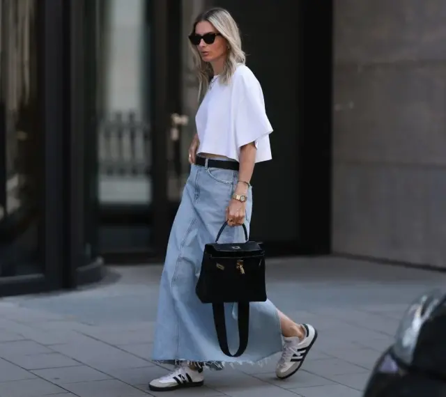 Kobieta w białej bluzce i długiej spódnicy jeansowej, z czarną torebką i sneakersami. Stylowe długa spódnica jeansowa stylizacje.