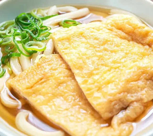 Pyszna zupa z makaronem udon z dwoma kawałkami smażonego tofu i zieloną cebulką.