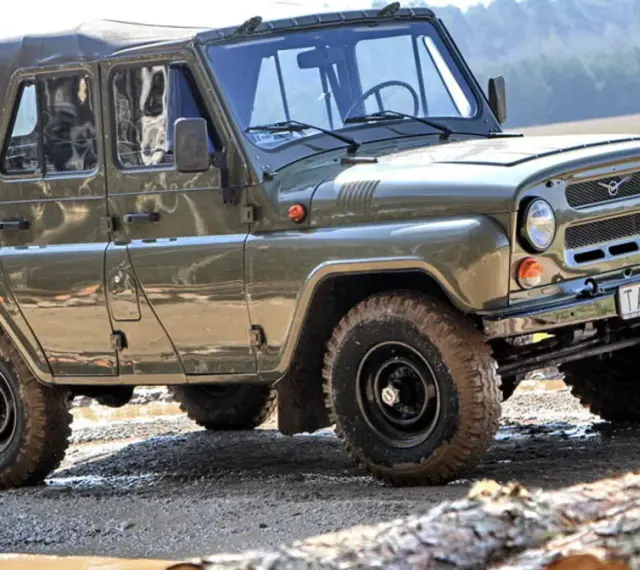 Zielony UAZ z plandeką, marka samochodu na u, pokonuje błotnisty teren.