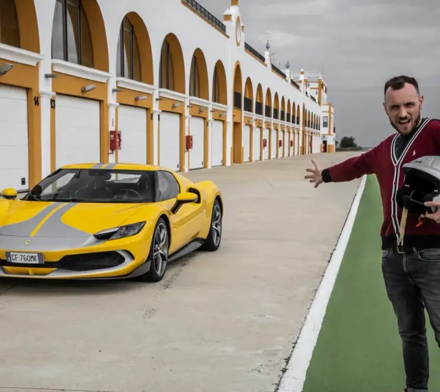 Żółte Ferrari 296 GTB z szarymi pasami na torze wyścigowym. Obok stoi mężczyzna z kaskiem, zapraszając do przejażdżki.
