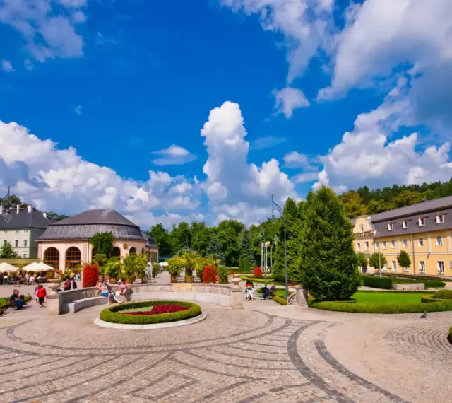 Słoneczny dzień w Kudowie Zdrój. Spacerowicze odpoczywają w pięknym parku zdrojowym, otoczonym zabytkową architekturą.