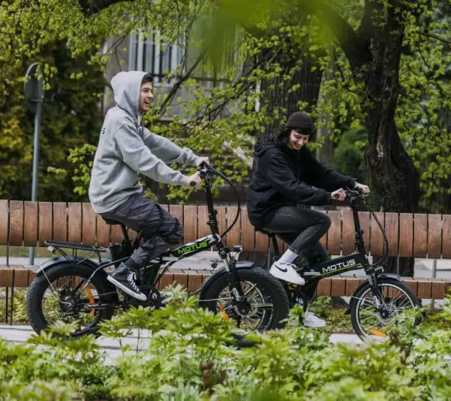 Dwaj młodzi ludzie cieszą się jazdą na rowerach elektrycznych. Dofinansowanie do roweru elektrycznego sprawia, że ekologiczny transport jest dostępny dla każdego.