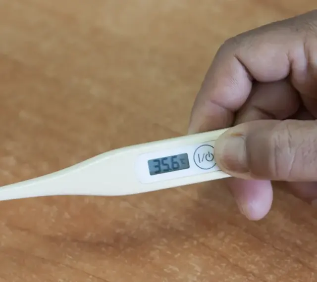 Dłoń trzyma termometr, który pokazuje 35.6°C. To niska temperatura, która może być objawem problemów zdrowotnych, np. podczas choroby covid.