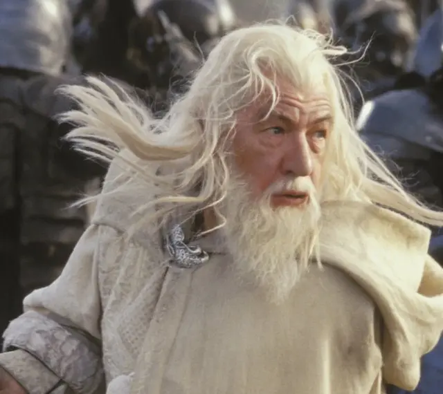 Gandalf z długą, siwą brodą i włosami, w białym płaszczu, gotowy do walki.