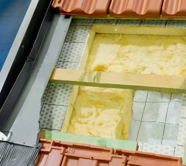 Wełna mineralna to świetny wybór, czym najlepiej ocieplić dom. Widoczna jest jej instalacja pod dachówką.