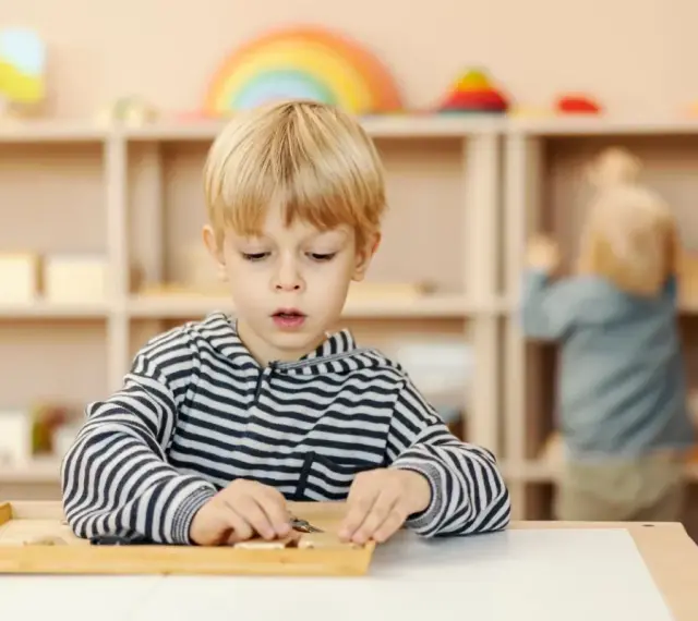 Chłopiec skupiony na zadaniu z materiałem Montessori. Ta metoda polega na samodzielnym odkrywaniu świata przez dziecko.