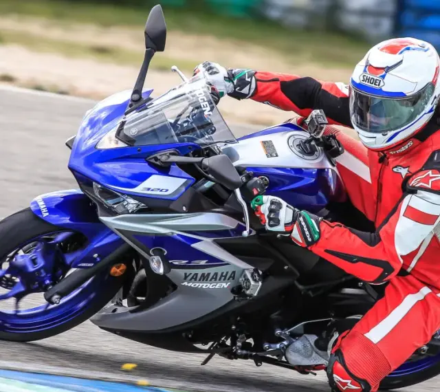Motocyklista w czerwonym kombinezonie i kasku ściga się na torze na motocyklu Yamaha R3.