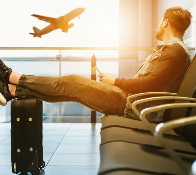 Mężczyzna z nogami na walizce czeka na lotnisku. Samolot startuje. Czyżby czekał na niego, czy to tylko efekt **overbooking**?