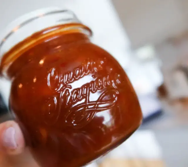 En hand håller ett glas med en mörkröd rabarber chutney.