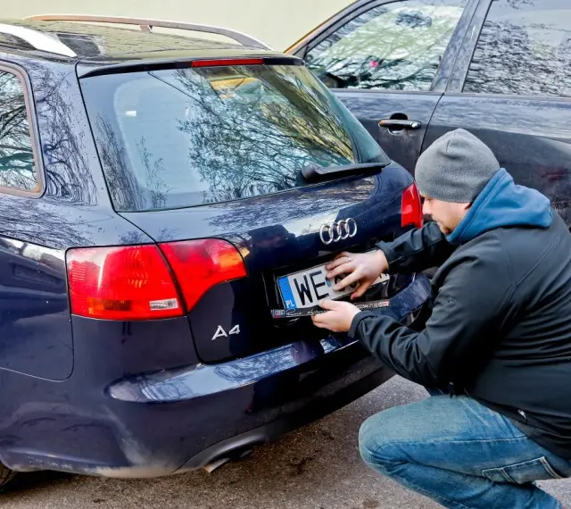 Mężczyzna montuje tablicę rejestracyjną na samochodzie Audi A4. Nowa rrs rejestracja gotowa do drogi.