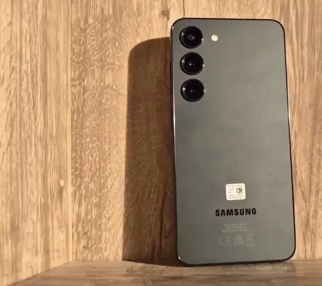 Szary Samsung S23 z trzema obiektywami aparatu na drewnianym tle. Długo działająca bateria pozwoli Ci cieszyć się nim przez cały dzień.