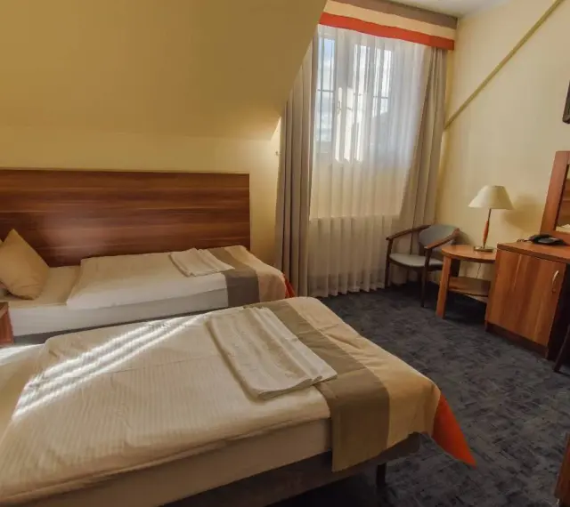 Pokój w zajazd u dziadka: dwa wygodne łóżka, stolik nocny z lampką, biurko z lustrem i krzesłem, telewizor.