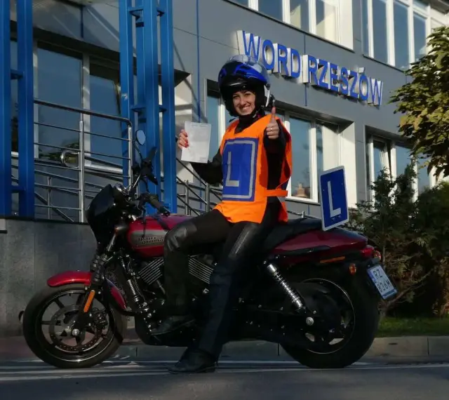 Szczęśliwa kursantka z prawem jazdy kat. A na motocyklu, w kamizelce z literą L, przed budynkiem WORD.
