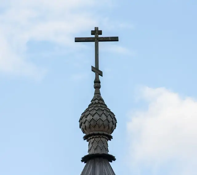 Drewniany krzyż prawosławny na tle błękitnego nieba z chmurami.