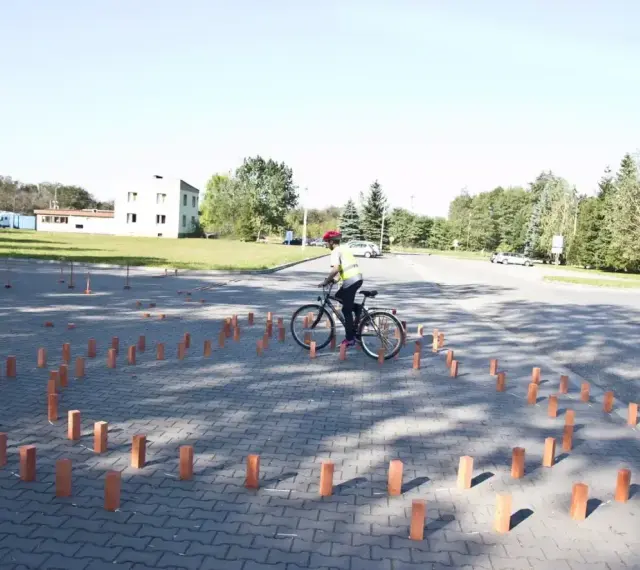 Młody rowerzysta w kamizelce odblaskowej i kasku pokonuje tor przeszkód z palików, przygotowując się do egzaminu na kartę rowerową.