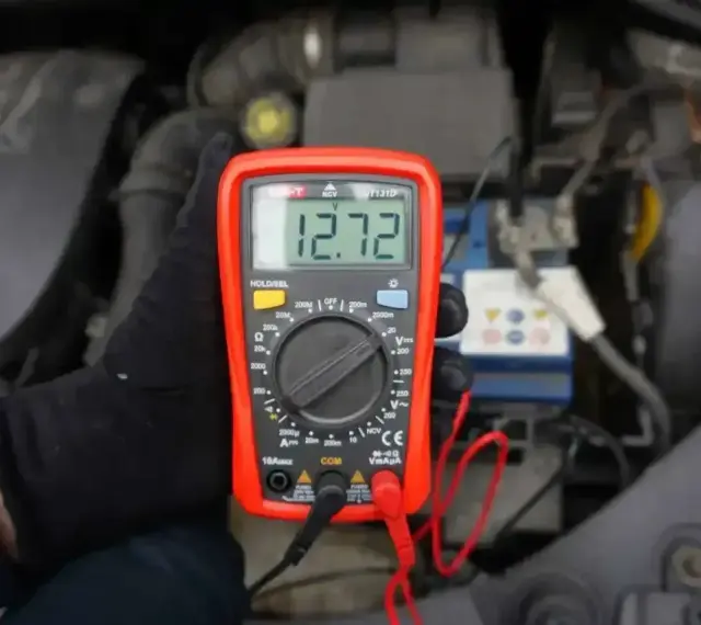 Multimetr pokazuje 12.72V, co oznacza prawidłowe napięcie akumulatora. Sprawdzanie stanu baterii przed podróżą.