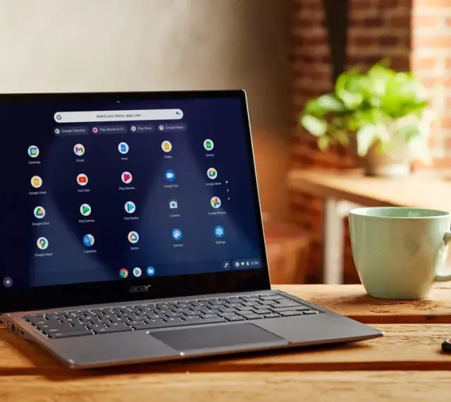 Laptop z systemem Chrome OS Flex na drewnianym stole, obok kubek i klucze.