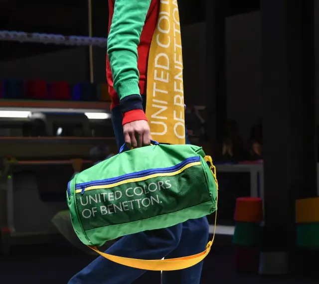 Zielony worek z napisem "UNITED COLORS OF BENETTON" niesiony przez modela w kolorowym swetrze.