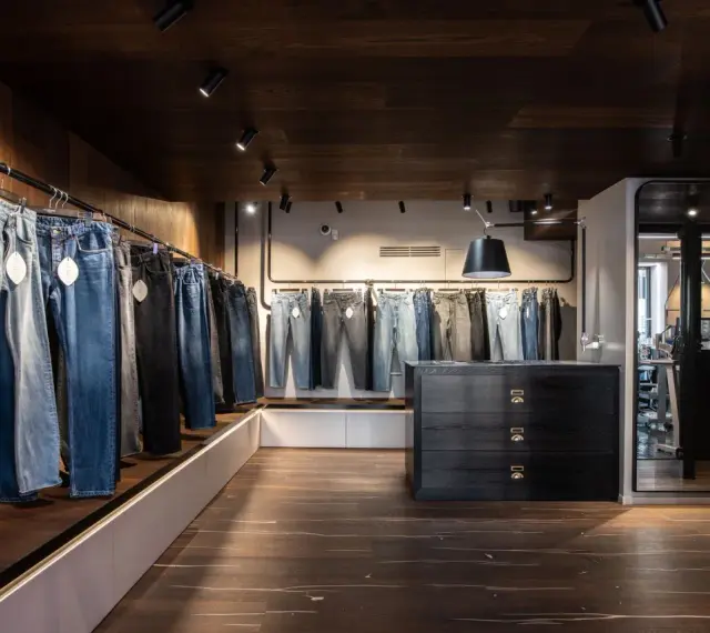 Jeans in vari lavaggi e tagli, inclusi modelli slim fit, esposti in un negozio moderno con pavimenti in legno scuro e illuminazione a faretti.