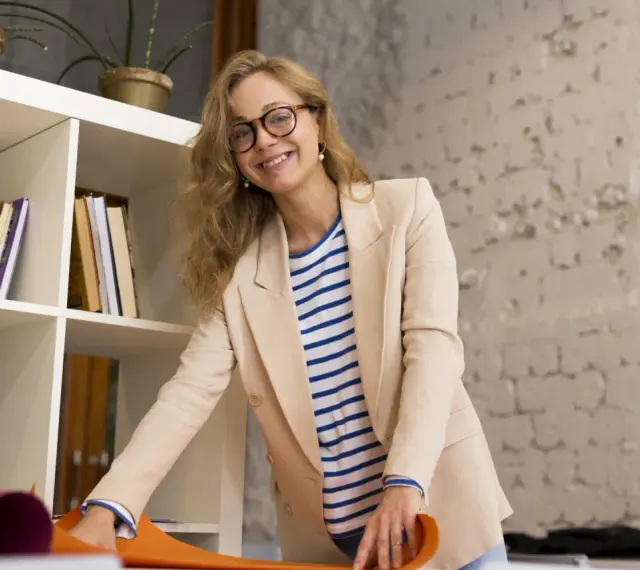 Uśmiechnięta kobieta w beżowej marynarce i pasiastym T-shircie, z okularami na nosie. Jej strój to przykład profesjonalnego dress code nauczyciela.