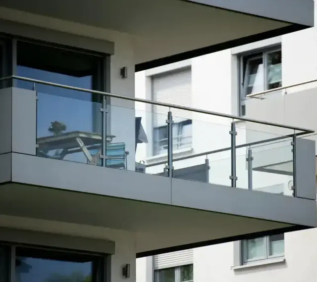 Nowoczesna loggia z przeszkloną balustradą, na której stoi stolik z kwiatami i krzesło.
