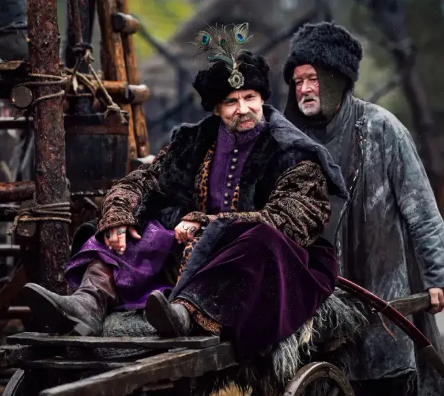 Bogaty pan w purpurowym stroju i futrzanej czapie z pawim piórem, siedzi na wozie. Czy to zapowiedź drugiego sezonu 1670?