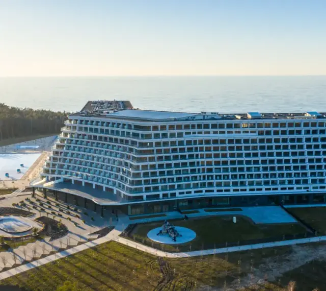 Nowoczesny, falisty pobierowo nowy hotel z basenami i widokiem na morze, otoczony lasem.