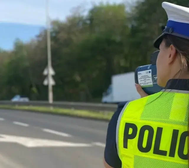 Policjantka w kamizelce odblaskowej mierzy prędkość pojazdów. Uważaj na tryb przyspieszony na drodze!