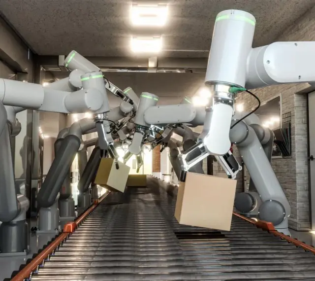 Wiele ramion robotów współpracujących chwyta kartony na linii produkcyjnej.