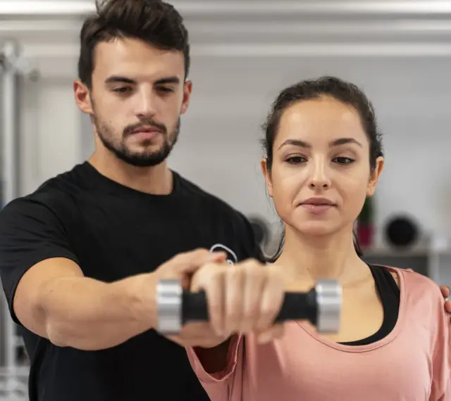 Trening dla początkujących: mężczyzna pomaga kobiecie podnosić hantle.
