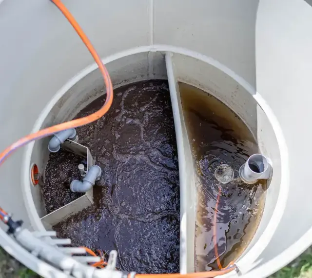 Wnętrze zbiornika biofos z ciemną wodą i rurami.