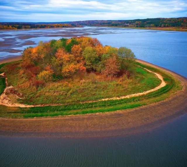 Jesienna wyspa na zalewie Brody, porośnięta kolorowymi drzewami i trawami, otoczona błękitną wodą.