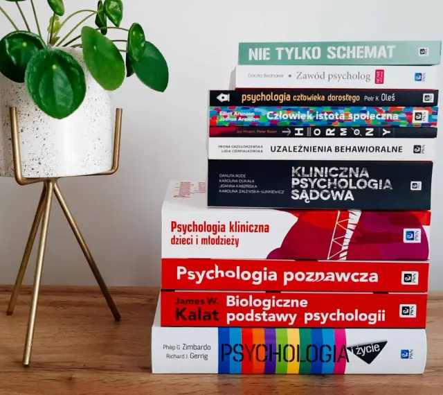 Stos książek o psychologii, od ogólnych po specjalistyczne, sugeruje, ile trwają studia psychologiczne. Obok zielona roślina.