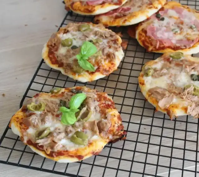 Kilka pysznych pizzett z tuńczykiem, oliwkami i bazylią na czarnej kratce.