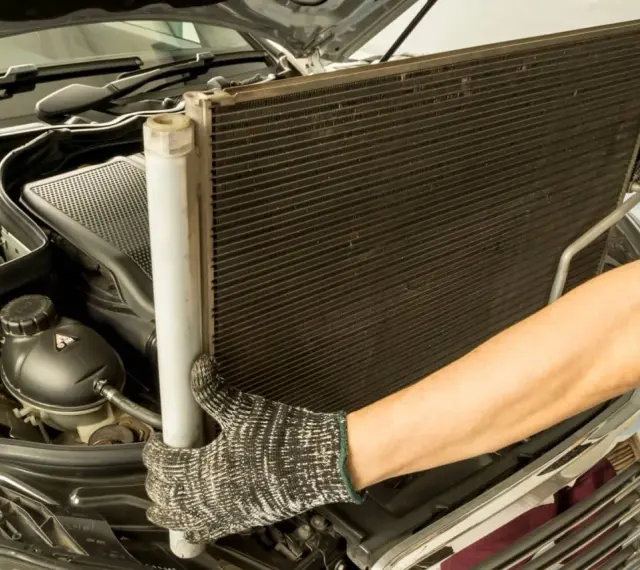 Mechanik w rękawicach wyjmuje chłodnicę klimatyzacji z silnika samochodu.