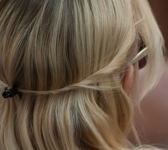 Piaskowy blond włosów spięty warkoczem z tyłu głowy. Delikatne pasma opadają na ramiona.