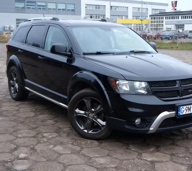 Czarny Dodge Journey 3.6 zaparkowany na placu z kostki brukowej. W tle budynki i inne samochody.