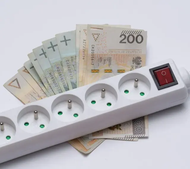 Pieniądze leżą pod listwą z gniazdkami, symbolizując zamrożenie cen prądu.