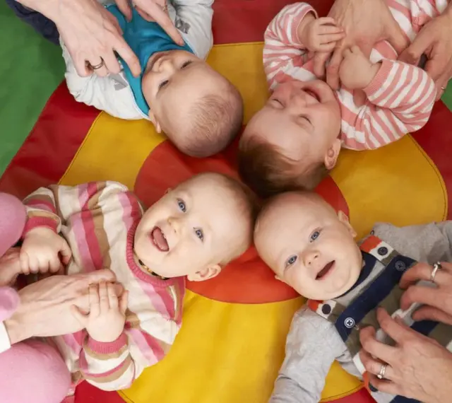 Uśmiechnięte dzieci na kolorowej macie. Czy żłobek jest dobry dla dziecka? Wiele maluchów wesoło bawi się z opiekunami.
